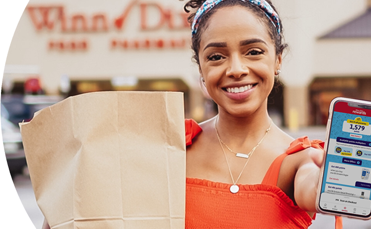 Woman smiling outside of a Winn-Dixie holding a grocery bag and phone with Winn-Dixie app