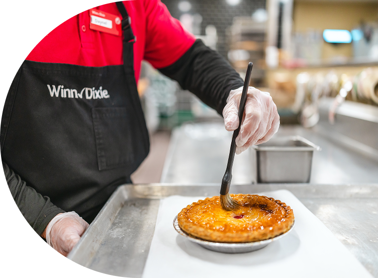 A Winn-Dixie associate in an apron carefully sets a pastry on a plate, showcasing their baking skills in a cozy kitchen environment.