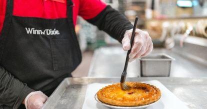 A Winn-Dixie associate in an apron carefully sets a pastry on a plate, showcasing their baking skills in a cozy kitchen environment.