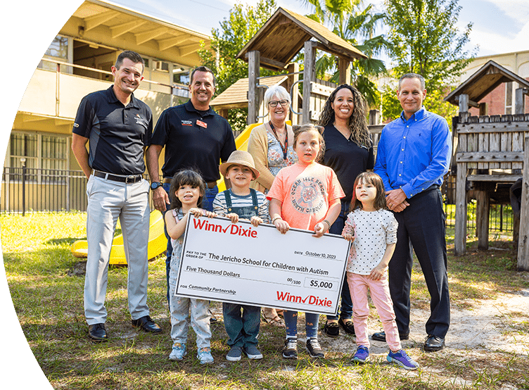 Group of Southeastern Grocers associates standing next to teachers from The Jericho School for Children with Autism. In front of them are young students holding a big $5,000 check.