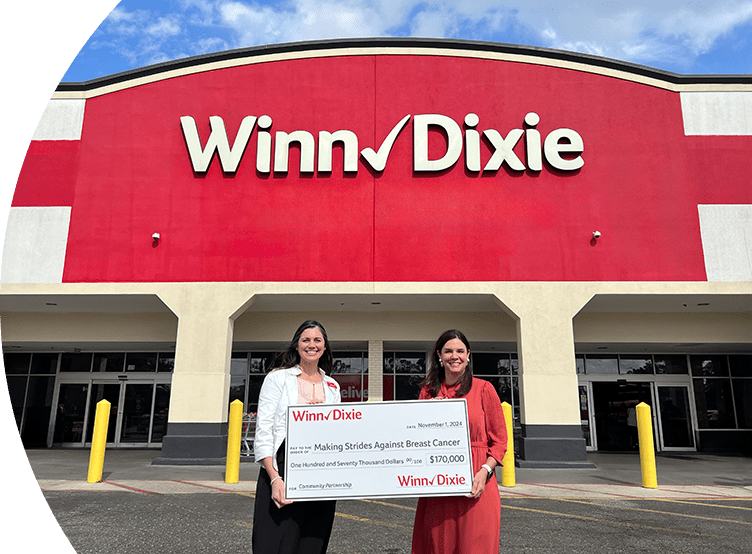 Two women standing outside of a Winn-Dixie holding a donation check for Making Strides Against Breast Cancer