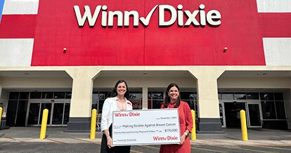 Two women standing outside of a Winn-Dixie holding a donation check for Making Strides Against Breast Cancer
