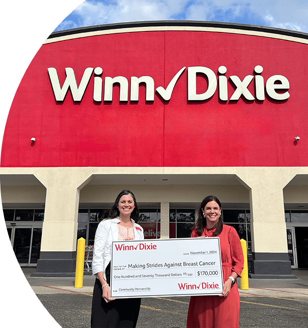 Two women standing outside of a Winn-Dixie holding a donation check for Making Strides Against Breast Cancer