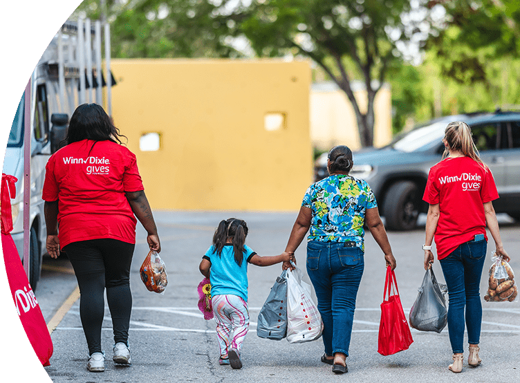 Two Winn-Dixie volunteers with a mom and a daughter carrying groceries