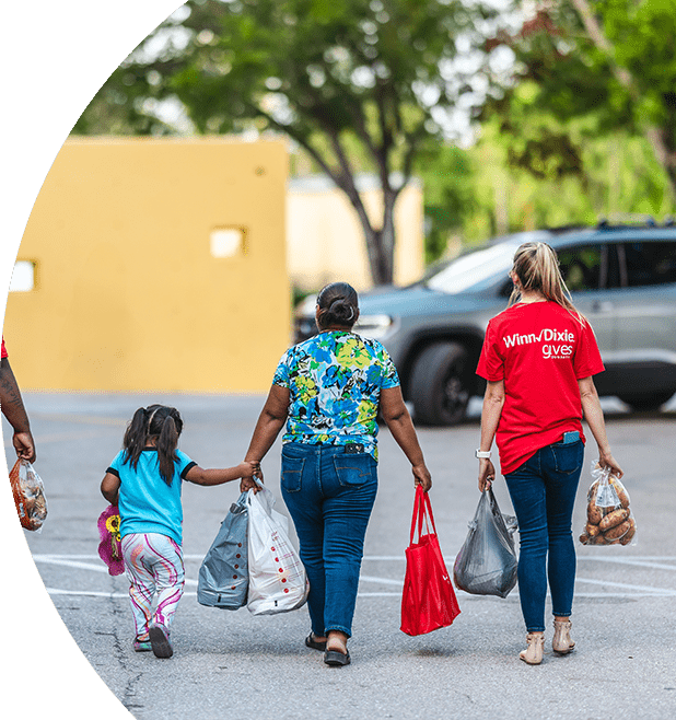 Two Winn-Dixie volunteers with a mom and a daughter carrying groceries