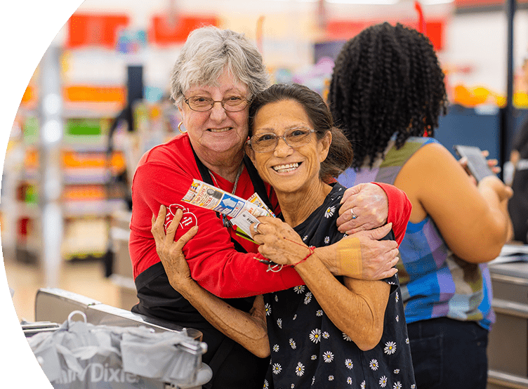 Winn-Dixie associate embracing smiling customer holding coupons.