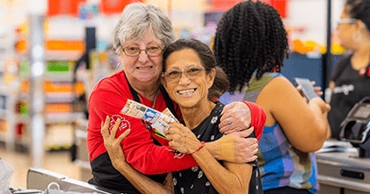 Winn-Dixie associate embracing smiling customer holding coupons.