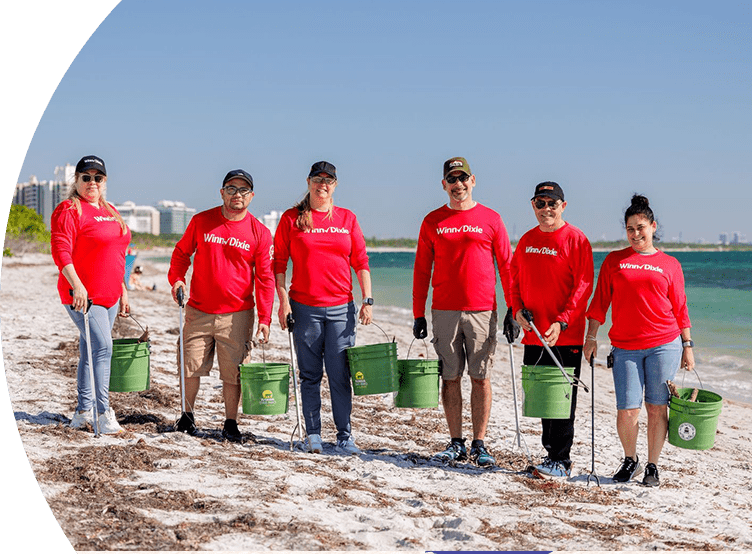 Winn-Dixie volunteers pick up debris at the beach. They are holding trash pickers and buckets.