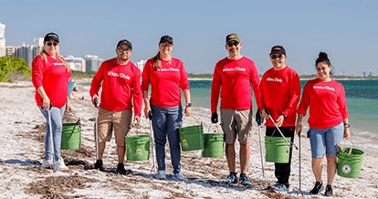 Winn-Dixie volunteers pick up debris at the beach. They are holding trash pickers and buckets.