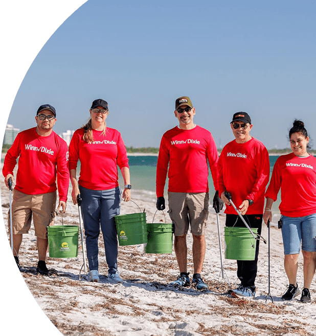 Winn-Dixie volunteers pick up debris at the beach. They are holding trash pickers and buckets.