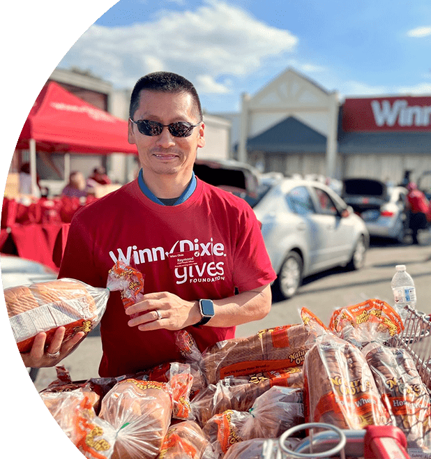 Raymond Rhee, Chief People Officer for Southeastern Grocers, wearing a Winn-Dixie Gives Foundation shirt. He is smiling while organizing food donations.