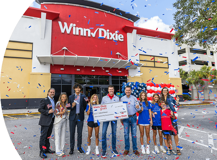 Group of people standing in front of a WInn-Dixie smiling. In the middle, three people are holding a big check for Folds of Honor.