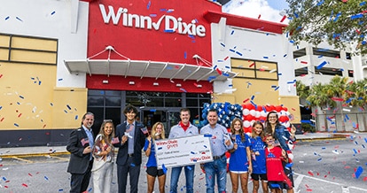 Group of people standing in front of a WInn-Dixie smiling. In the middle, three people are holding a big check for Folds of Honor.
