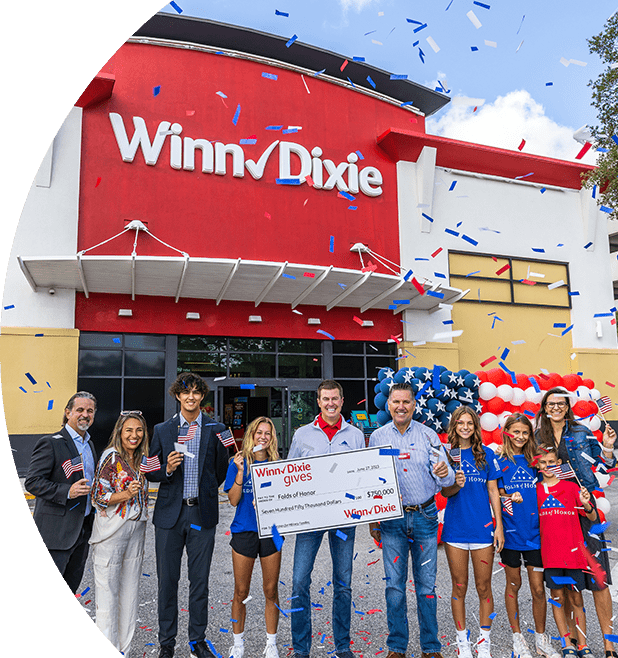 Group of people standing in front of a WInn-Dixie smiling. In the middle, three people are holding a big check for Folds of Honor.