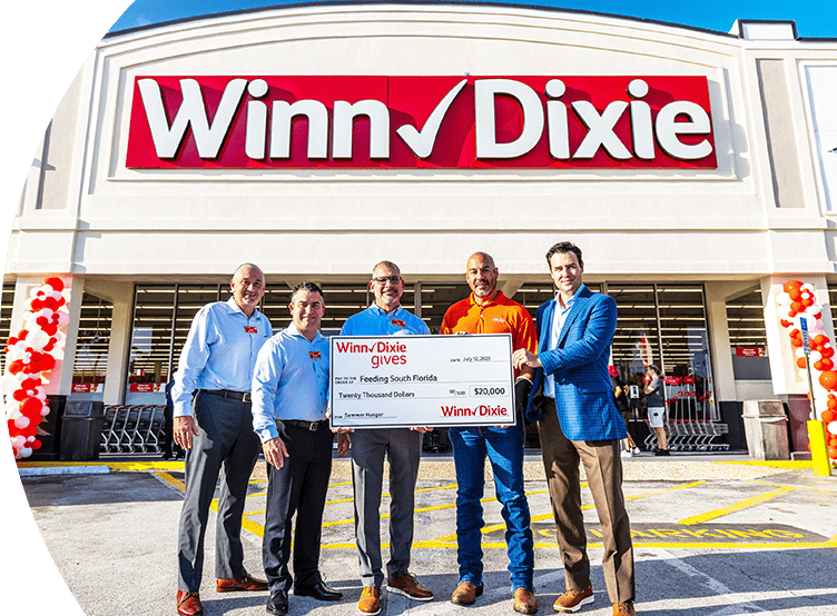 Winn-Dixie associates standing in front of a Winn-Dixie storefront holding a big $20,000 check for Feeding South Florida. 