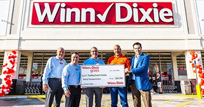 Winn-Dixie associates standing in front of a Winn-Dixie storefront holding a big $20,000 check for Feeding South Florida. 