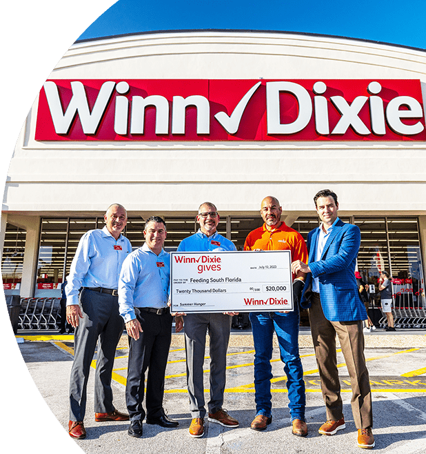 Winn-Dixie associates standing in front of a Winn-Dixie storefront holding a big $20,000 check for Feeding South Florida. 