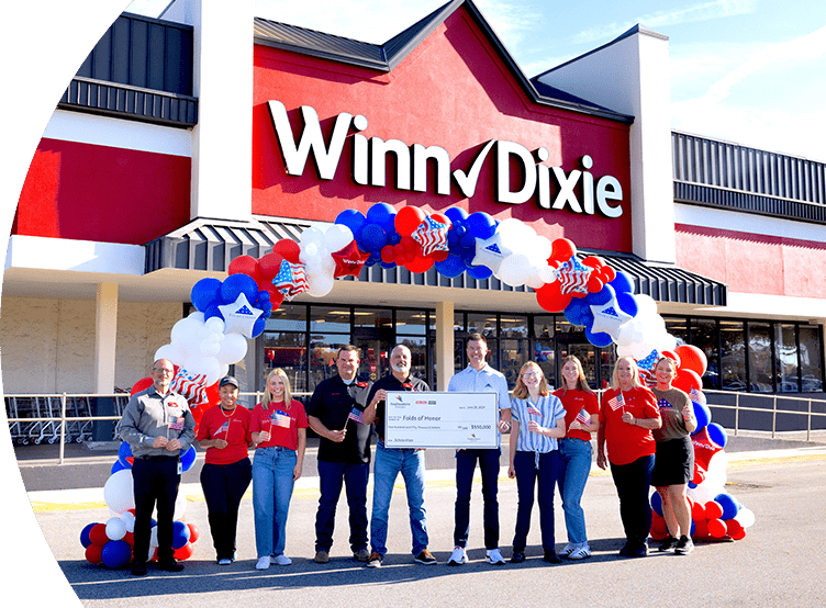 Group of SEG employees standing in front of a Winn-Dixie holding a large check.