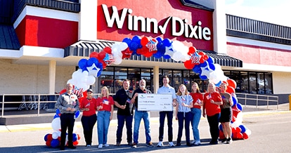 Group of SEG employees standing in front of a Winn-Dixie holding a large check.
