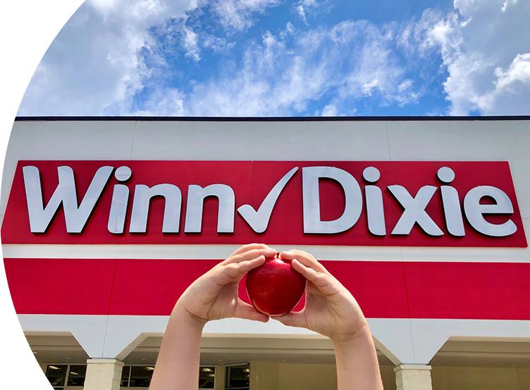Closeup of two hands in the shape of a heart holding an apple in front of a Winn-Dixie store