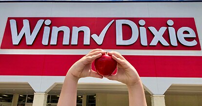 Closeup of two hands in the shape of a heart holding an apple in front of a Winn-Dixie store