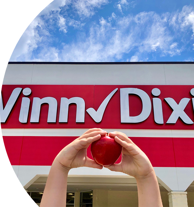 Closeup of two hands in the shape of a heart holding an apple in front of a Winn-Dixie store