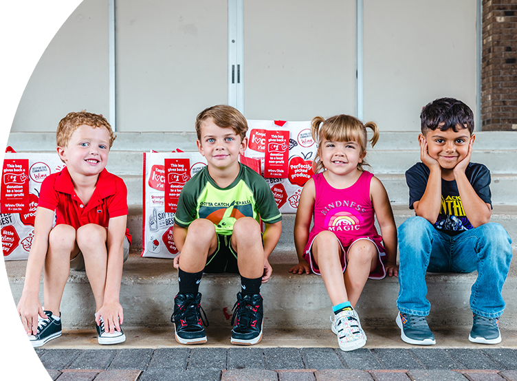 Four smiling kids sitting on steps. Behind them are three Winn-Dixie reusable bags.