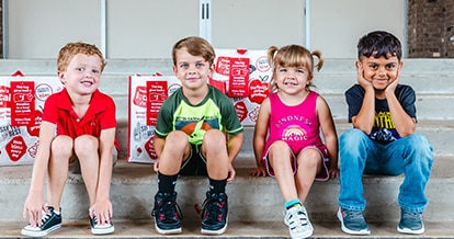 Four smiling kids sitting on steps. Behind them are three Winn-Dixie reusable bags.