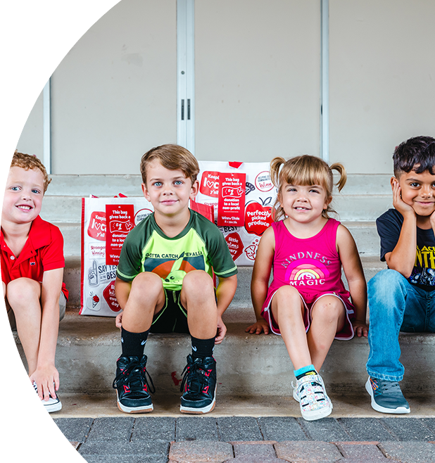 Four smiling kids sitting on steps. Behind them are three Winn-Dixie reusable bags.