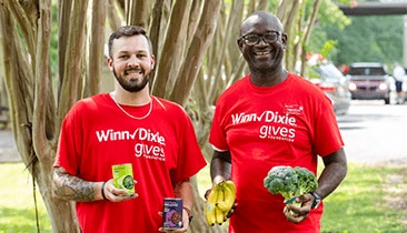 Gives Foundation volunteers joyfully holding canned goods and produce.
