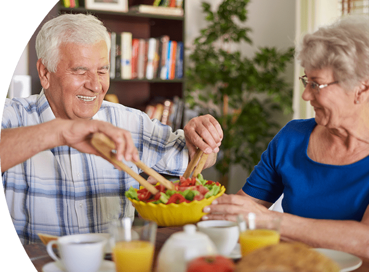 Older man and woman at the dinner table smiling eating a salad