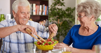 Older man and woman at the dinner table smiling eating a salad