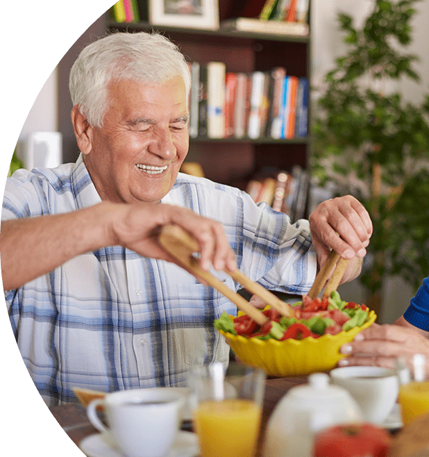 Older man and woman at the dinner table smiling eating a salad