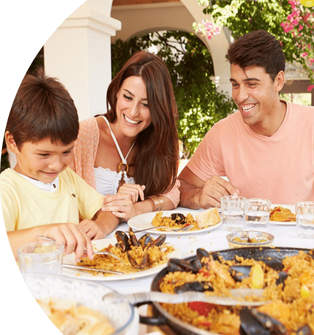 Smiling family sitting at the dinner table eating paella.