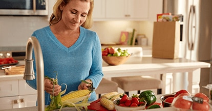 Image of a blonde woman shucking corn in a kitchen