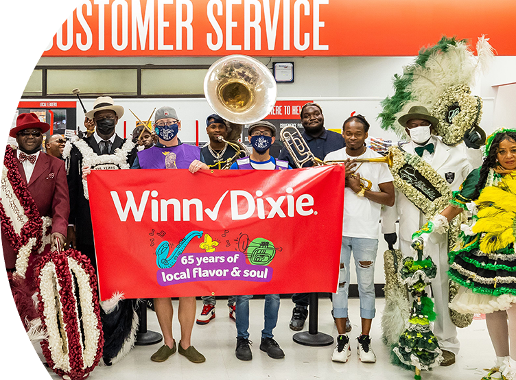 Festive crowd of people holding up a '65 years of local flavor and soul' Winn-Dixie banner