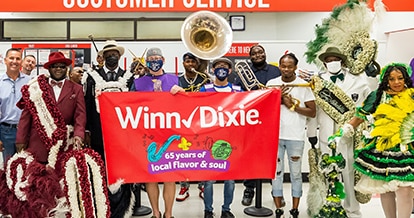 Festive crowd of people holding up a '65 years of local flavor and soul' Winn-Dixie banner