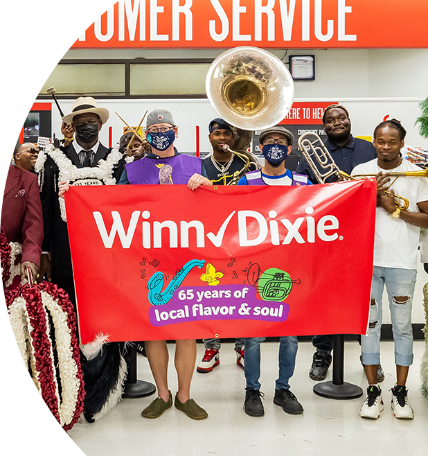 Festive crowd of people holding up a '65 years of local flavor and soul' Winn-Dixie banner