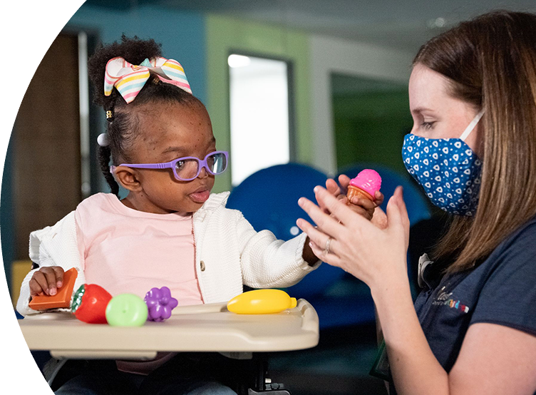 Small child sitting in a high top chair with produce toys on the tray and showing one to a nurse