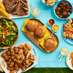 Delicious summer cook out items spread out on table including burgers, salad, vegetables, fries, and condiments.
