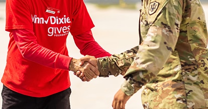 Individual wearing a Winn-Dixie gives Foundation shirt giving a handshake to a military service member in uniform.