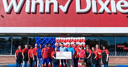 Group of people standing in front of a Winn-Dixie holding a Winn-Dixie gives jumbo check for Folds of Honor