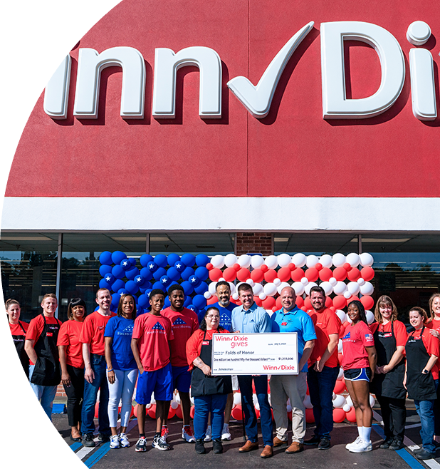 Group of people standing in front of a Winn-Dixie holding a Winn-Dixie gives jumbo check for Folds of Honor